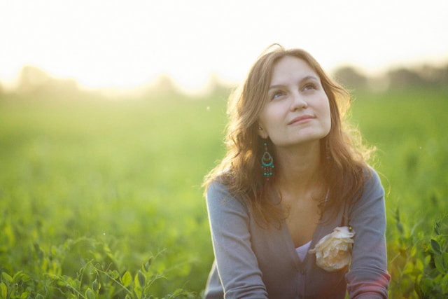 Contemplative woman enjoying a peaceful moment in a lush green field at sunset, reflecting a serene lifestyle and connection with nature
